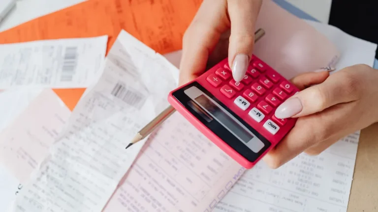 Hands using a pink calculator to manage expenses amidst various receipts and documents.