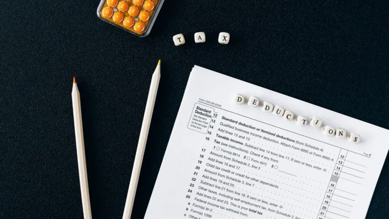 Flat lay of tax form, pencils, and calculator on black background, emphasizing tax deductions.