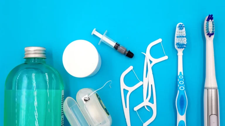 Flat lay of oral hygiene essentials including toothbrushes, floss, and mouthwash on a blue surface.