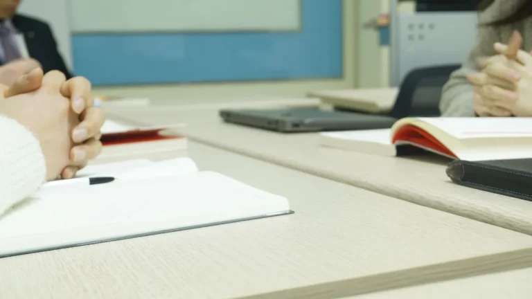 Close-up of a professional meeting setup with hands, laptops, and notebooks on a wooden desk.