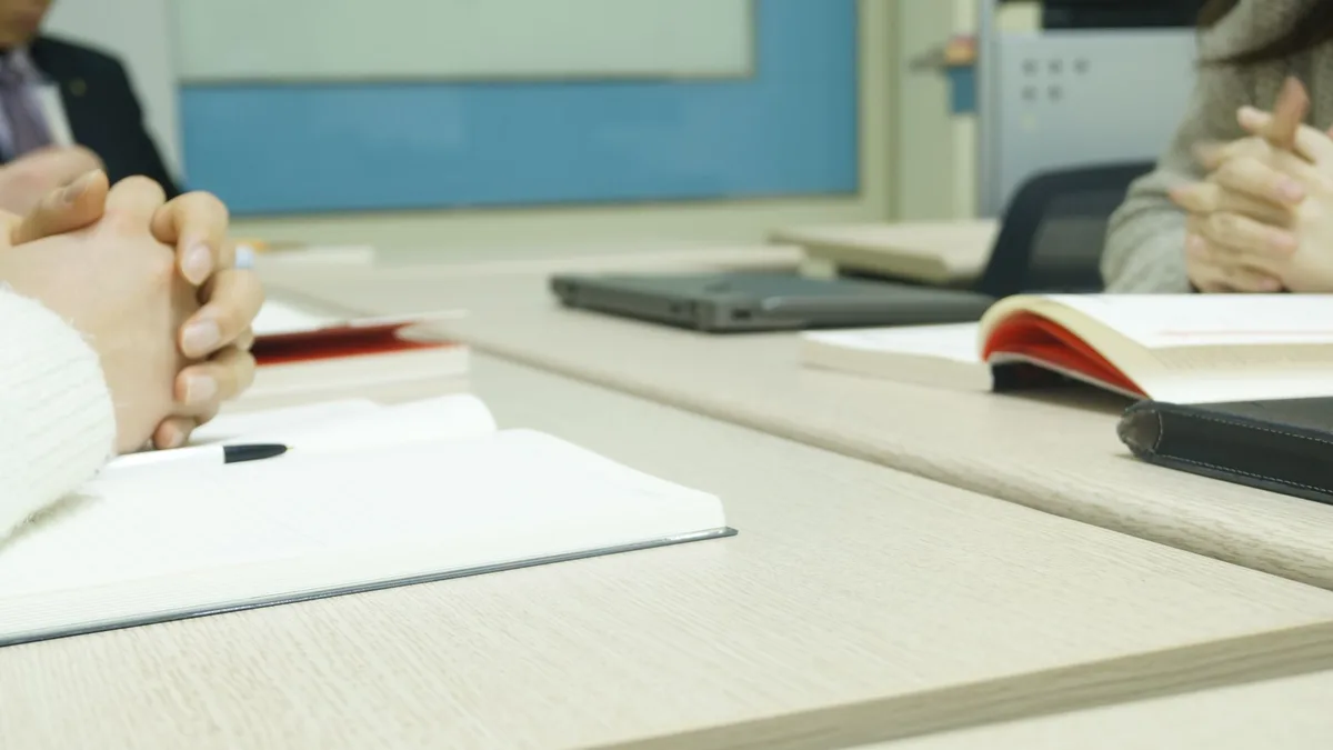 Close-up of a professional meeting setup with hands, laptops, and notebooks on a wooden desk.
