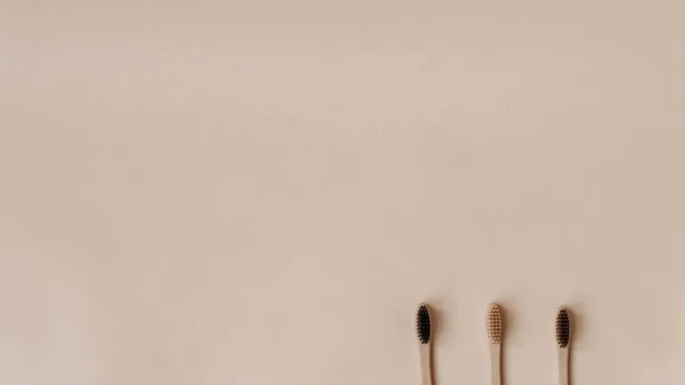 Three bamboo toothbrushes on a minimal beige background promoting eco-friendly oral care.