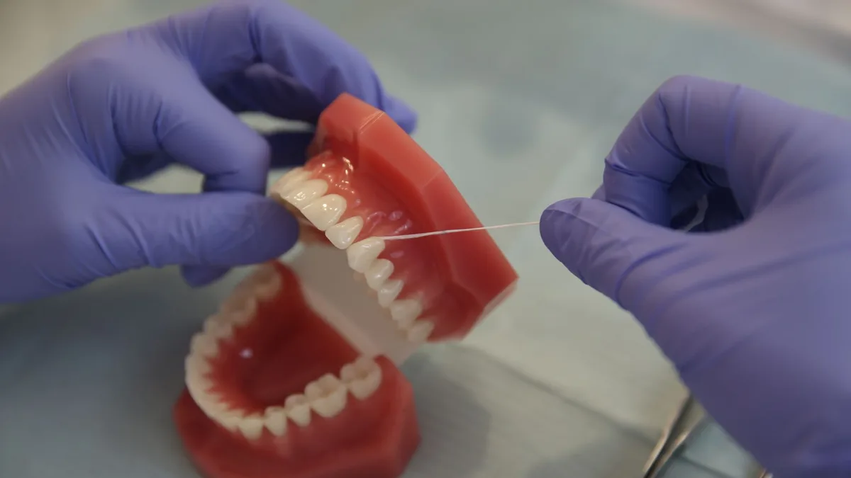 Close-up of a dental professional using floss on a denture model, emphasizing hygiene.