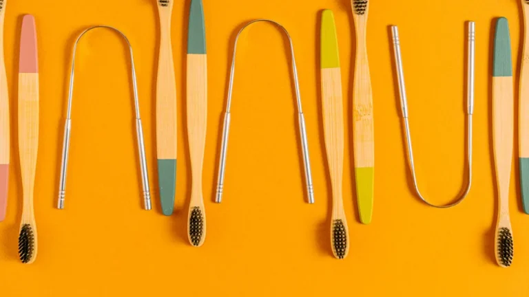 Artistic arrangement of bamboo toothbrushes and tongue scrapers on an orange surface, highlighting eco-friendly oral care.