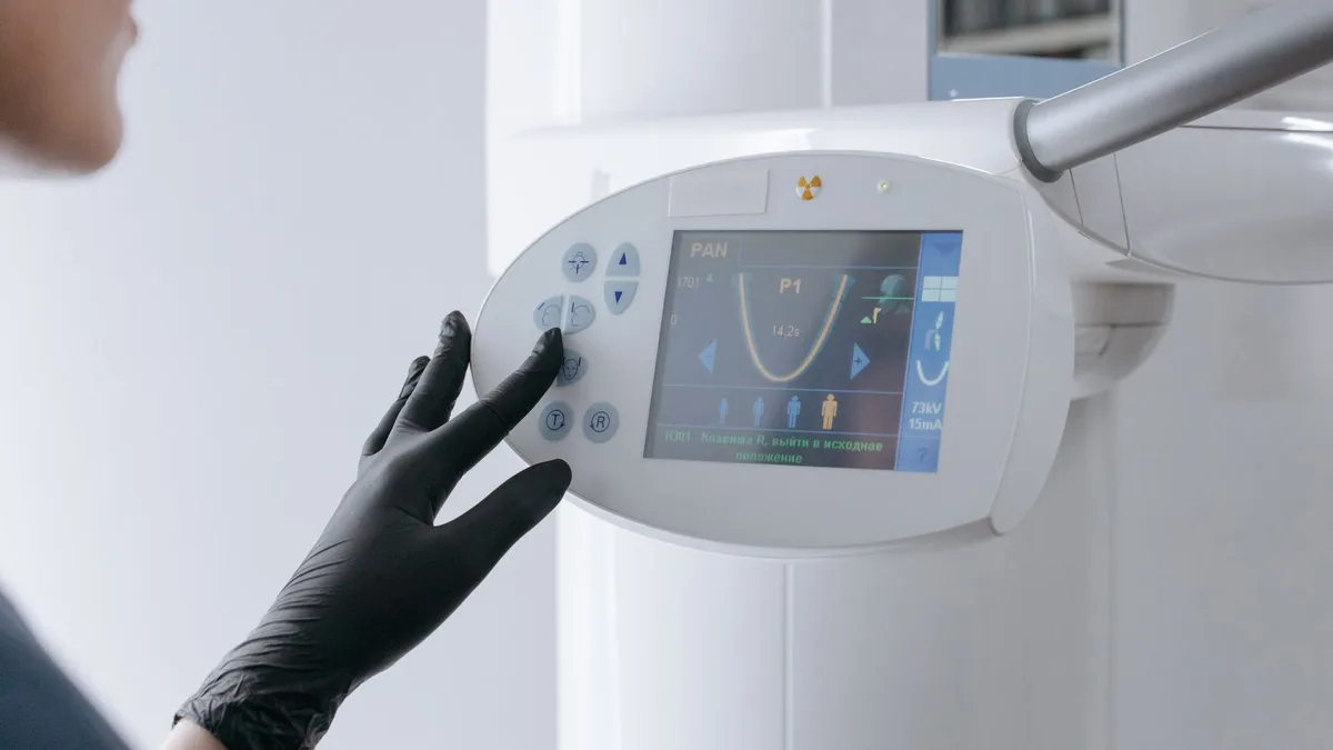 Close-up of a dental equipment screen being operated by a gloved hand in a clinic setting.