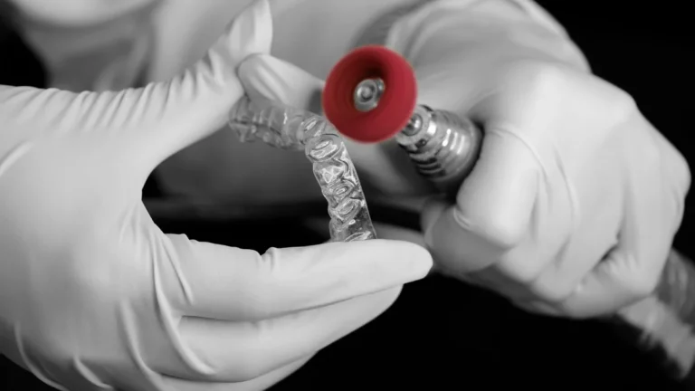A dental technician uses a grinder to polish a clear aligner in a laboratory setting.