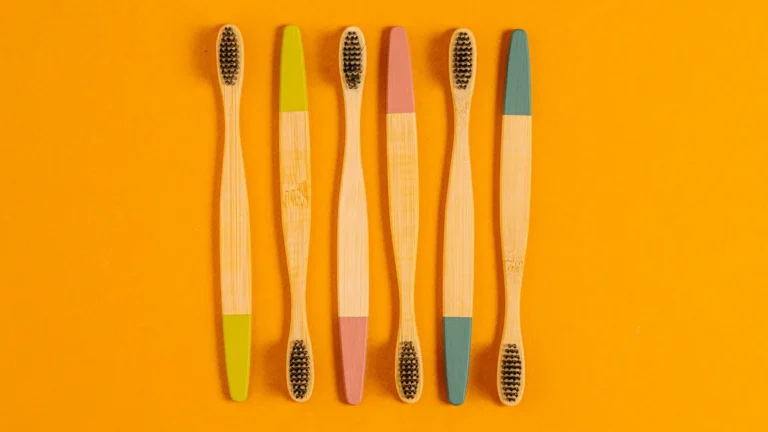 Six bamboo toothbrushes with colorful tips on a vibrant orange surface.