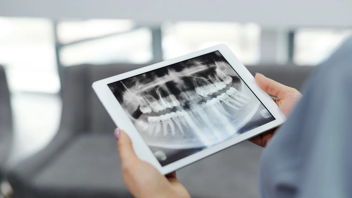 Close-up of hands holding a tablet displaying a dental X-ray indoors.