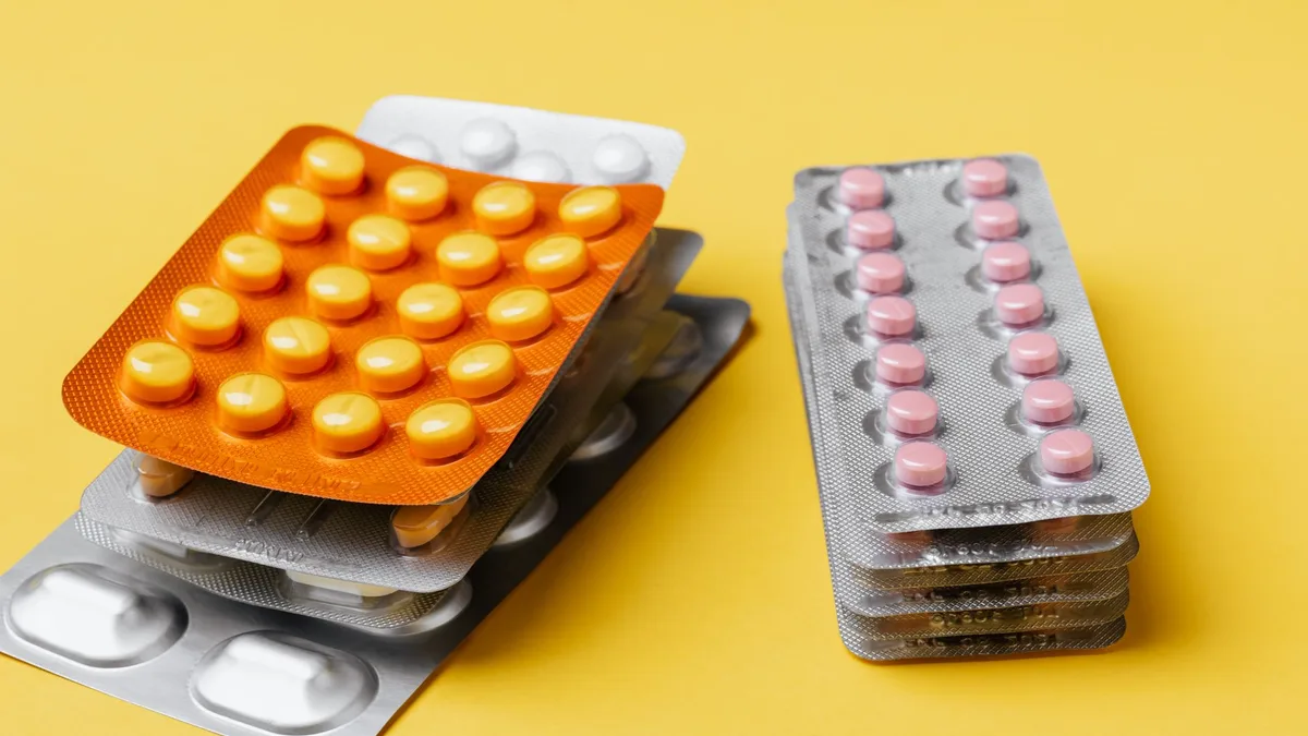 Heaps of various medication pills of different color and shape in blister packs placed on bright yellow background