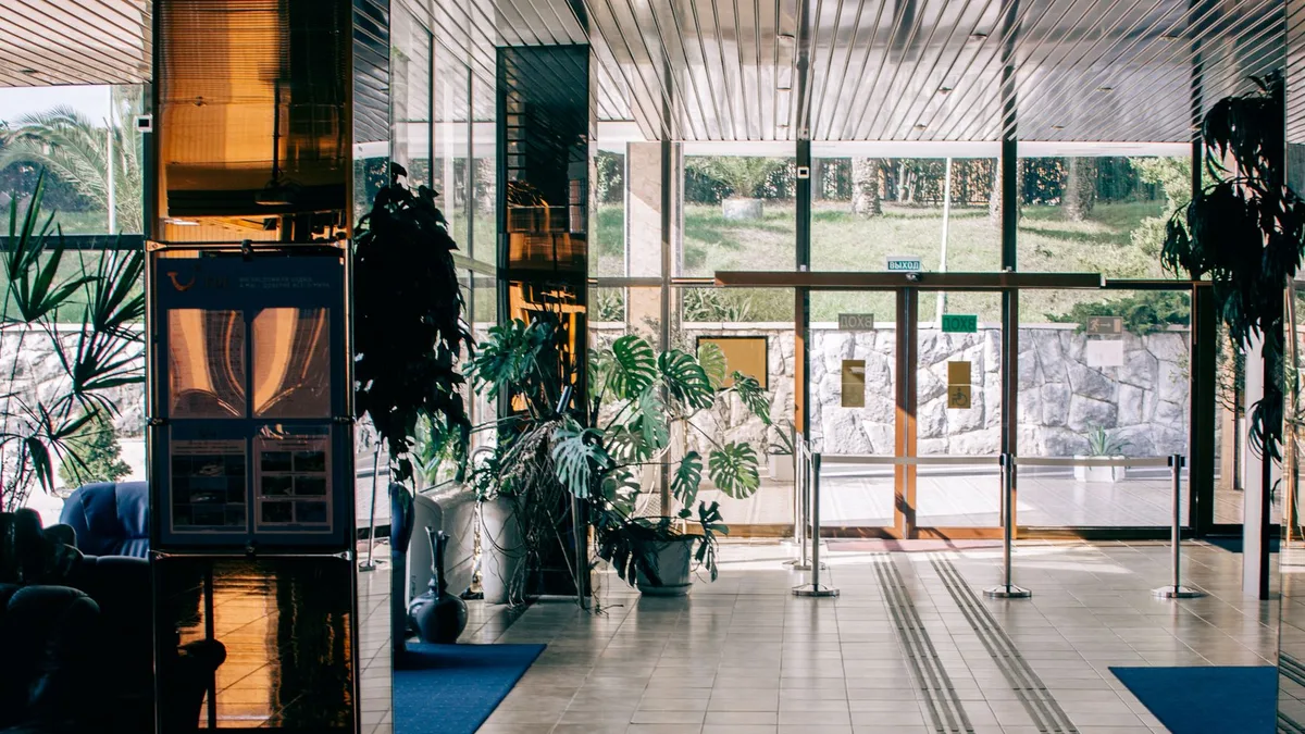 Elegant modern hotel lobby with glass entrance, luxurious design, and indoor plants.