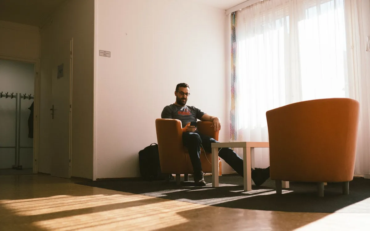 Mężczyzna siedzi spokojnie w fotelu w słonecznej poczekalni i patrzy w telefon