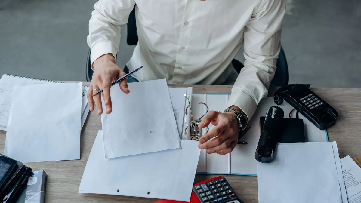 A business professional organizing documents at a busy office desk, emphasizing productivity.