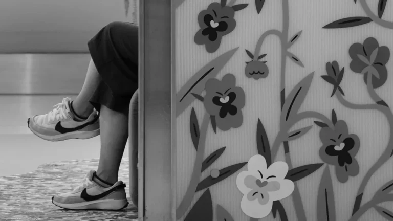 Black and white image of crossed legs behind a floral-patterned screen.