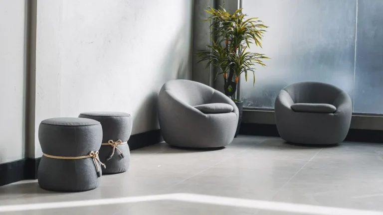 Minimalist room featuring contemporary gray chairs, a plant, and soft lighting through large windows.