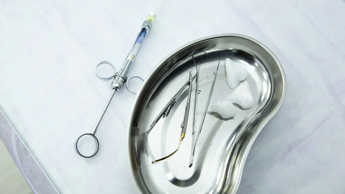 A set of sterile medical tools and syringe displayed in a kidney tray for dental or surgical use.