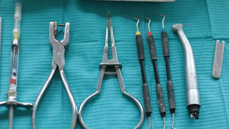Close-up of dental tools on a teal cloth, including syringe, pliers, and scaler.