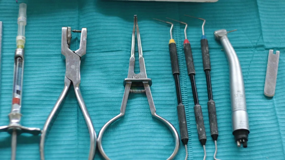 Close-up of dental tools on a teal cloth, including syringe, pliers, and scaler.