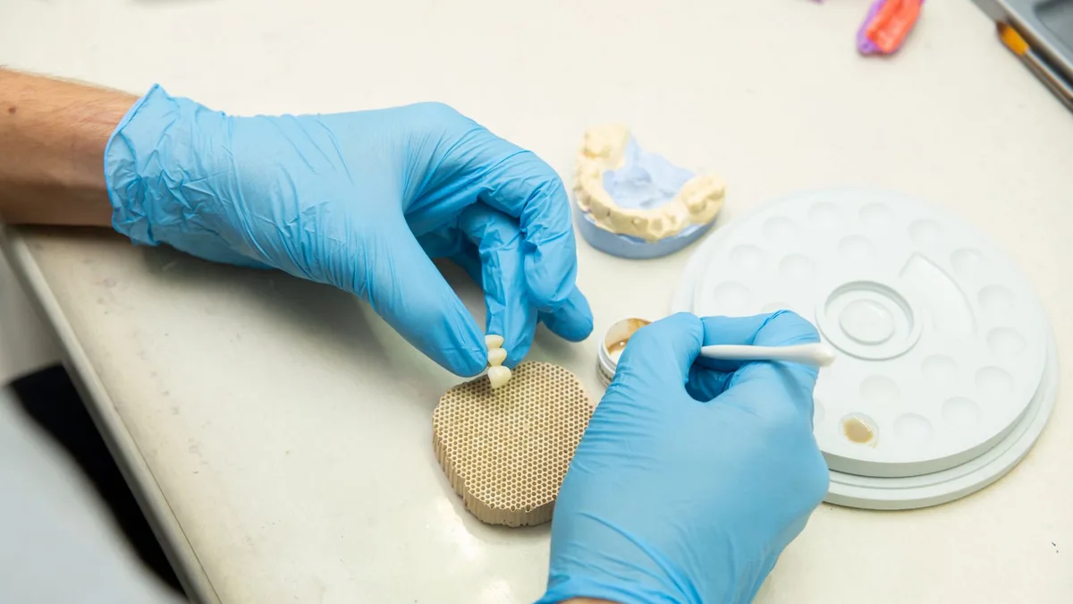 From above of crop anonymous orthodontist in latex gloves creating fake teeth for denture while sitting at table in light dental clinic