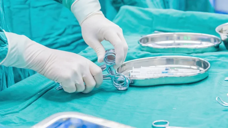 Close-up of a surgeon's gloved hands arranging instruments on a tray in an operating room.