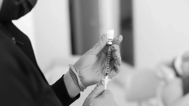A close-up black and white photo of a medical professional preparing an injection in a clinic setting.