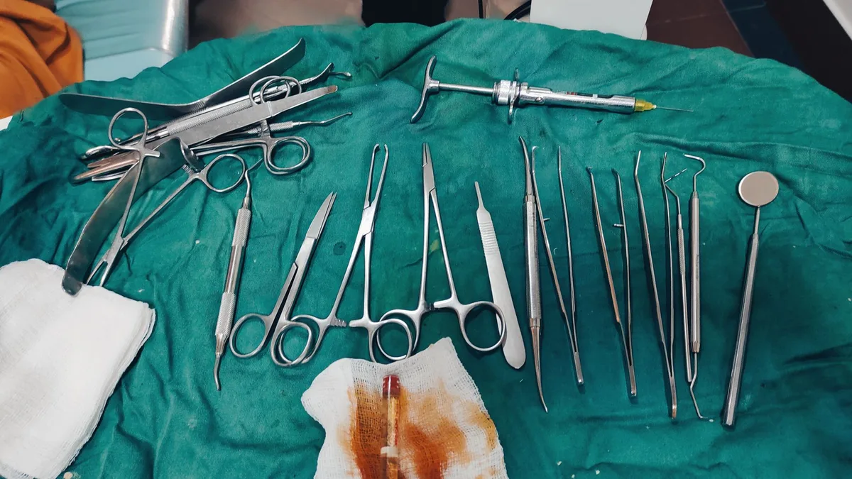 Close-up view of surgical tools arranged on green medical drapes in a clinical setting.