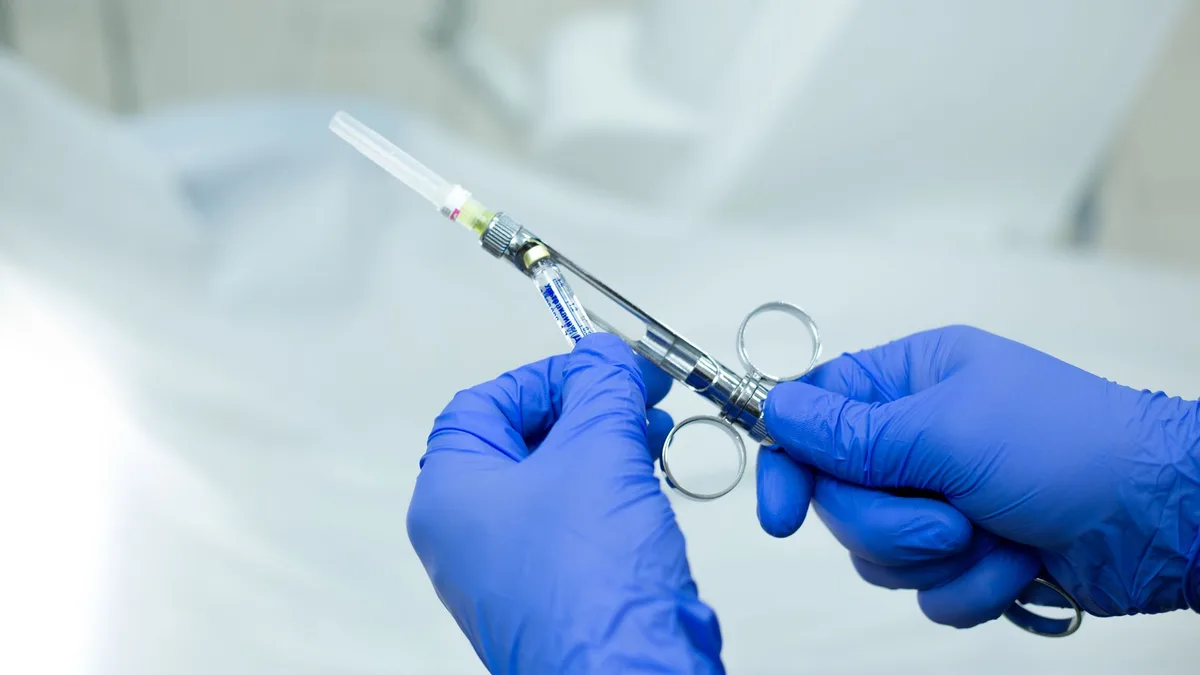A close-up of gloved hands holding a sterile medical syringe in a healthcare setting.